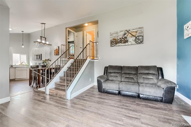 living room with an inviting chandelier, high vaulted ceiling, sink, and light hardwood / wood-style floors