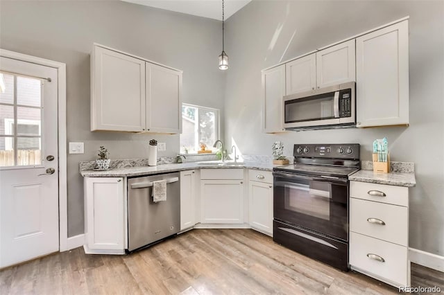 kitchen with sink, white cabinetry, decorative light fixtures, light wood-type flooring, and stainless steel appliances