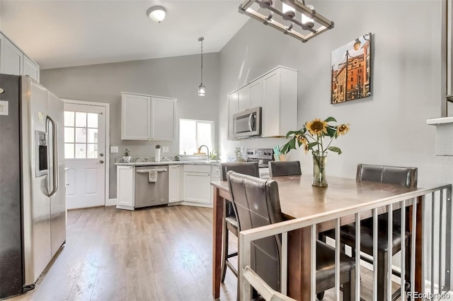 kitchen with sink, white cabinets, hanging light fixtures, stainless steel appliances, and light wood-type flooring