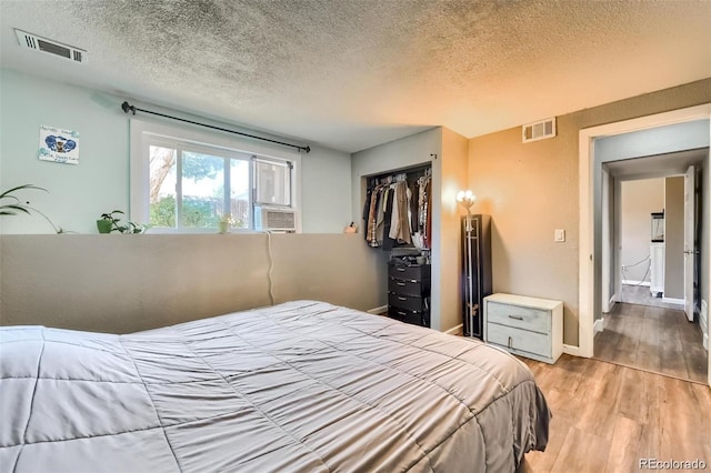 bedroom with cooling unit, light hardwood / wood-style flooring, a closet, and a textured ceiling