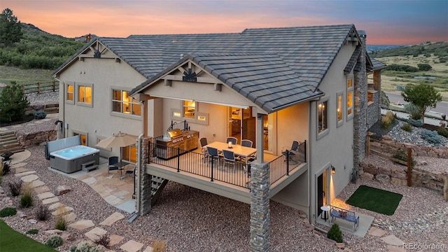 back house at dusk featuring a patio area and a hot tub