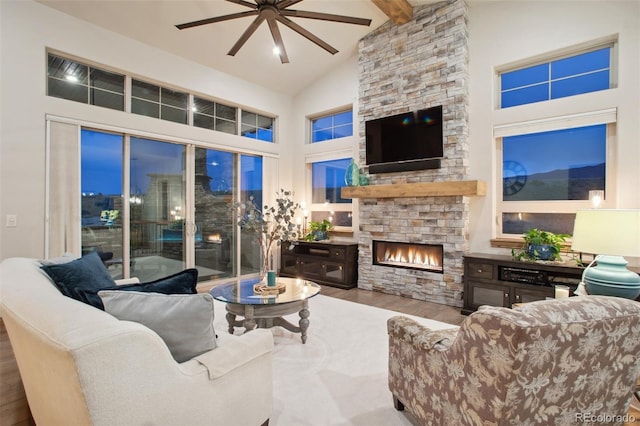 living room featuring high vaulted ceiling, wood-type flooring, ceiling fan, a stone fireplace, and beam ceiling