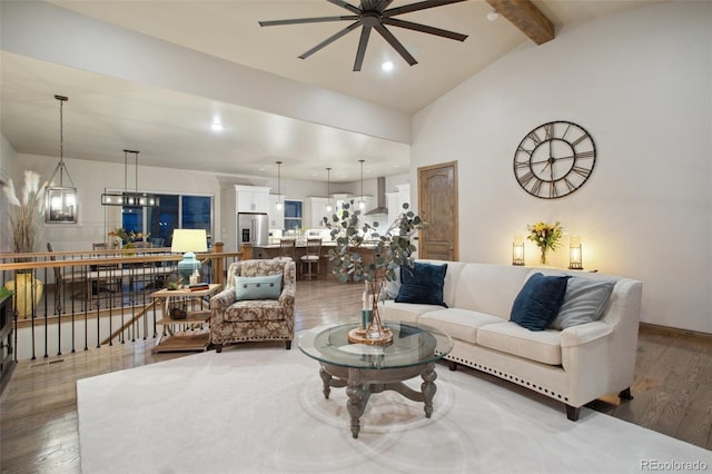 living room featuring ceiling fan with notable chandelier, dark wood-type flooring, and vaulted ceiling with beams