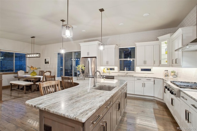 kitchen featuring white cabinets, stainless steel appliances, a large island with sink, sink, and pendant lighting