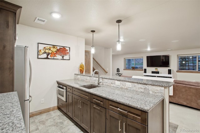 kitchen featuring light stone countertops, stainless steel appliances, sink, pendant lighting, and dark brown cabinetry