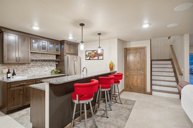 kitchen featuring light stone countertops, stainless steel fridge, dark brown cabinets, decorative light fixtures, and a breakfast bar