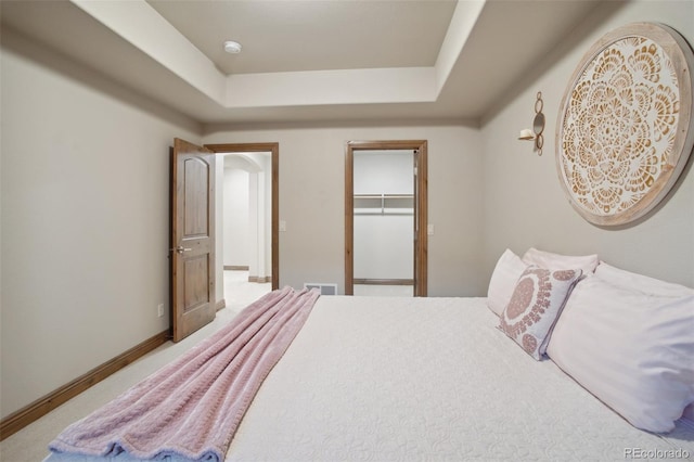 carpeted bedroom with a walk in closet, a raised ceiling, and a closet