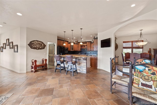 28098 Green Valley Ln, Conifer, CO 80433 - kitchen featuring arched walkways, backsplash, a kitchen island with sink, a breakfast bar area, and stone tile flooring