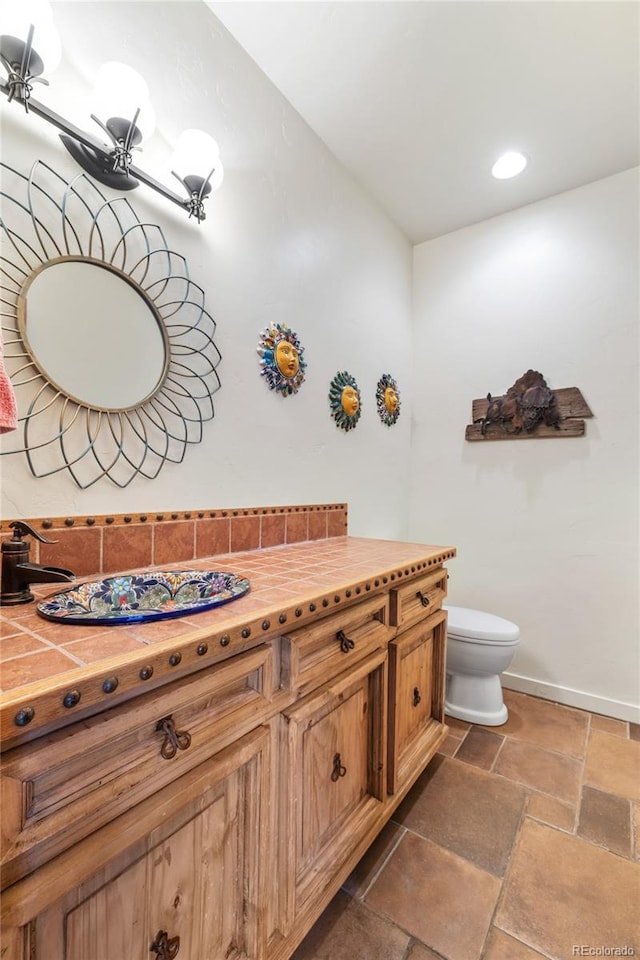 28098 Green Valley Ln, Conifer, CO 80433 - bathroom with toilet, vanity, stone tile floors, baseboards, and recessed lighting