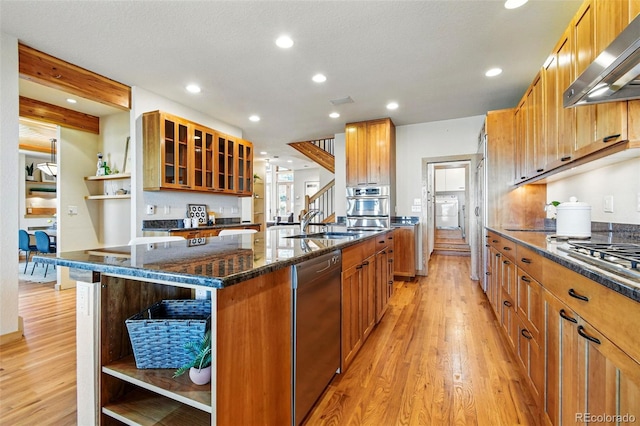 9041 Eastridge Rd, Golden, CO 80403 - kitchen with open shelves, wall chimney exhaust hood, appliances with stainless steel finishes, light wood-style floors, and a kitchen island with sink