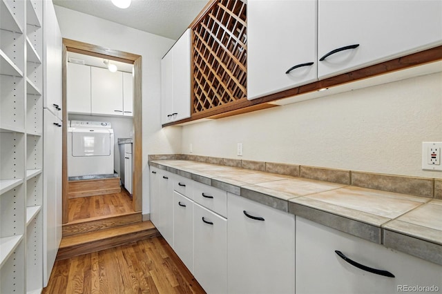 9041 Eastridge Rd, Golden, CO 80403 - kitchen with washer / clothes dryer, wood finished floors, white cabinets, and tile counters