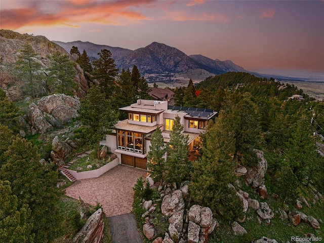 9041 Eastridge Rd, Golden, CO 80403 - back of property at dusk featuring a balcony, driveway, roof mounted solar panels, a mountain view, and a sunroom