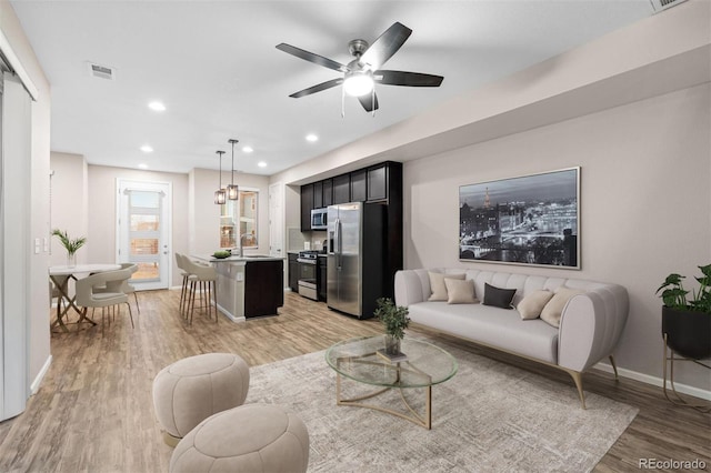 living room featuring ceiling fan, sink, and light hardwood / wood-style flooring