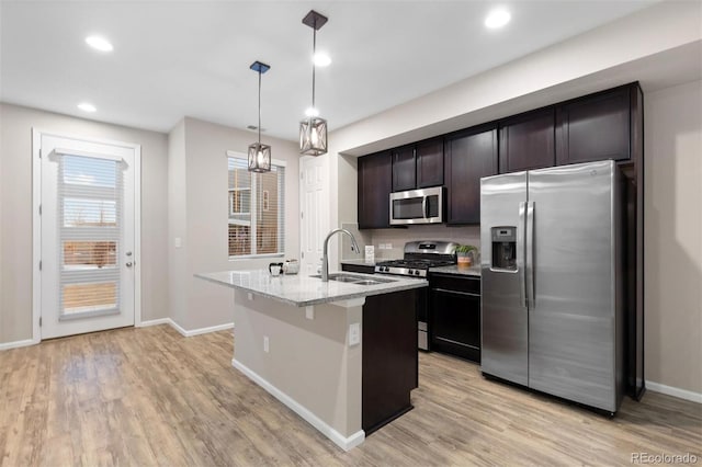 kitchen featuring light stone countertops, stainless steel appliances, sink, hanging light fixtures, and an island with sink