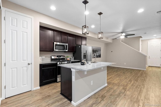 kitchen featuring decorative backsplash, appliances with stainless steel finishes, light stone countertops, ceiling fan, and a center island with sink