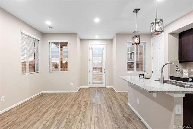 kitchen with decorative backsplash, light wood-type flooring, sink, hanging light fixtures, and a breakfast bar area