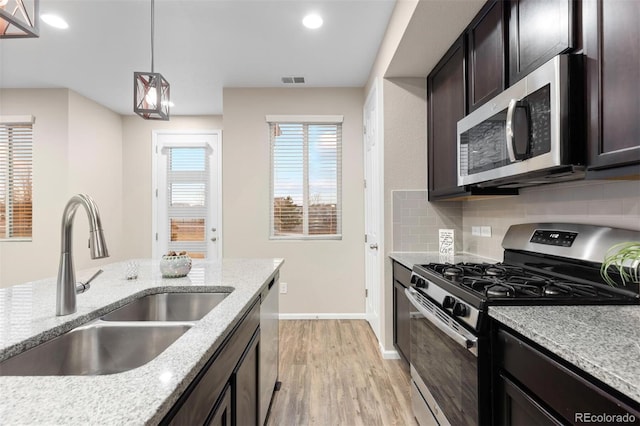 kitchen with hanging light fixtures, sink, decorative backsplash, appliances with stainless steel finishes, and light stone counters