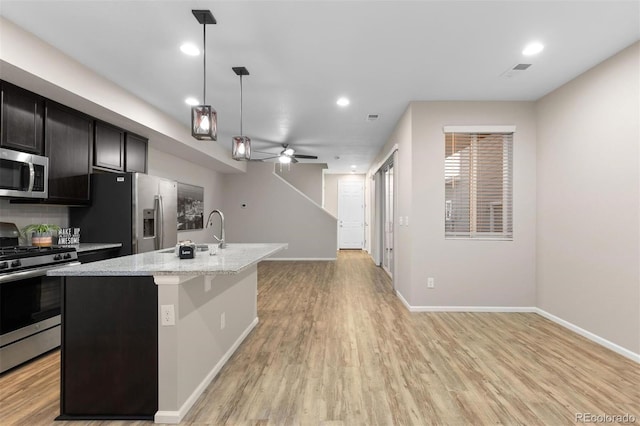 kitchen with light stone countertops, appliances with stainless steel finishes, ceiling fan, pendant lighting, and a center island with sink