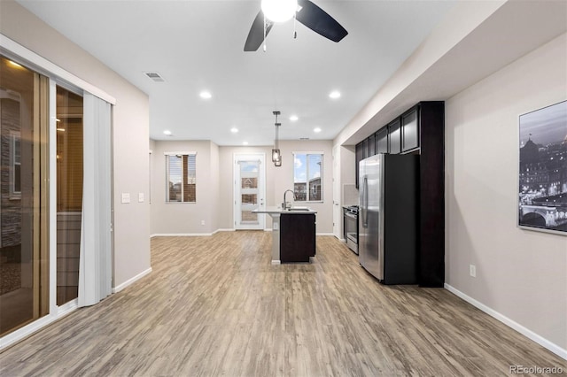 kitchen featuring sink, light wood-type flooring, an island with sink, decorative light fixtures, and stainless steel appliances