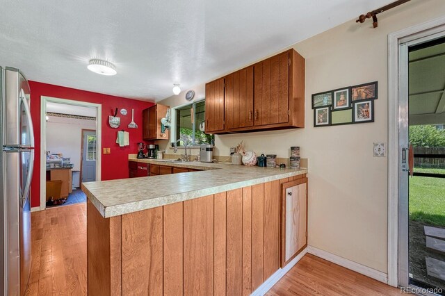 7479 Pierce St, Arvada, CO 80003 - kitchen with freestanding refrigerator, a peninsula, light wood-style flooring, light countertops, and brown cabinetry