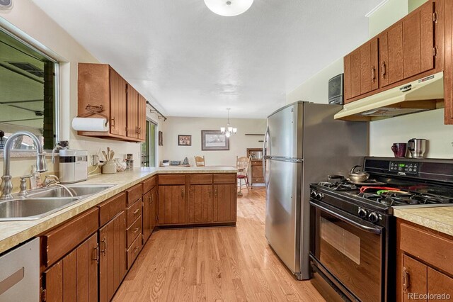 7479 Pierce St, Arvada, CO 80003 - kitchen with black gas stove, under cabinet range hood, light wood-style flooring, light countertops, and a chandelier
