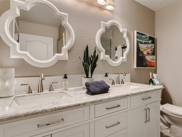 bathroom featuring a textured wall, a sink, toilet, and double vanity