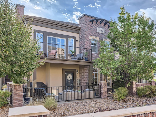 view of front of home with brick siding, a balcony, and stucco siding