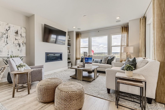 17719 Prairie Peak Trl, Parker, CO 80134 - living room with built in shelves, light wood-style floors, a glass covered fireplace, baseboards, and recessed lighting