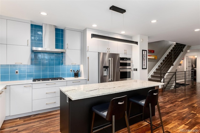 kitchen with stainless steel appliances, a center island, white cabinets, decorative light fixtures, and wall chimney exhaust hood