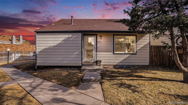 view of front of property featuring entry steps, a yard, a shingled roof, and fence