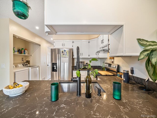 1247 S Idalia St, Aurora, CO 80017 - kitchen featuring appliances with stainless steel finishes, separate washer and dryer, under cabinet range hood, white cabinetry, and dark stone counters