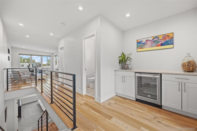 bar featuring white cabinetry, beverage cooler, and light hardwood / wood-style flooring