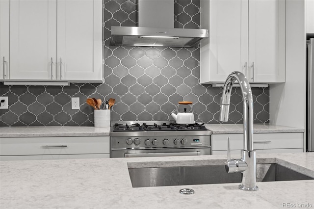 kitchen featuring stainless steel gas stove, white cabinets, backsplash, and wall chimney exhaust hood