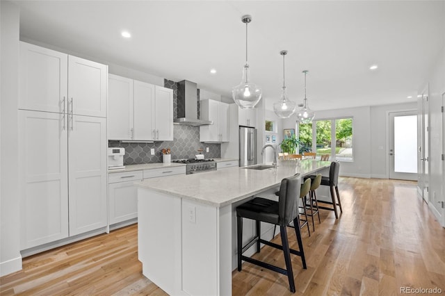 kitchen featuring white cabinetry, appliances with stainless steel finishes, pendant lighting, a kitchen island with sink, and wall chimney range hood