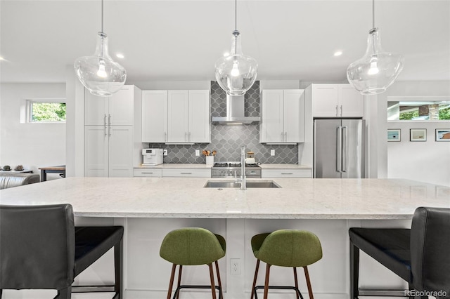 kitchen with white cabinets, high end refrigerator, wall chimney exhaust hood, and a spacious island