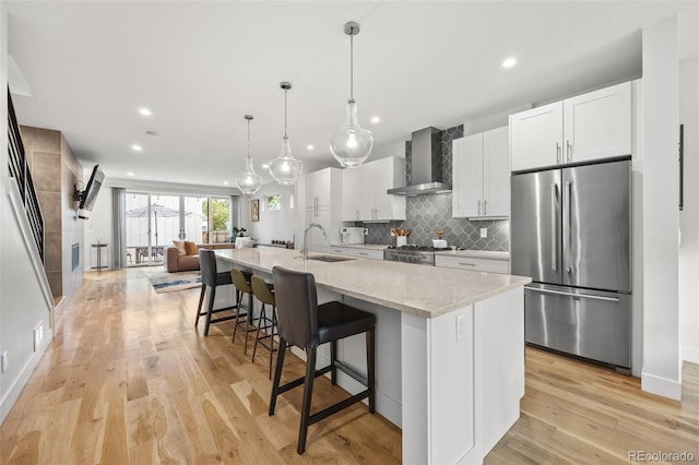 kitchen featuring a center island with sink, appliances with stainless steel finishes, wall chimney range hood, and white cabinets