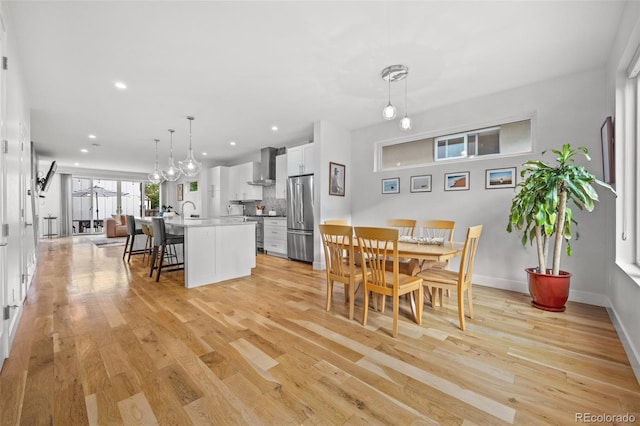 kitchen featuring an island with sink, a kitchen breakfast bar, hanging light fixtures, high end appliances, and wall chimney range hood