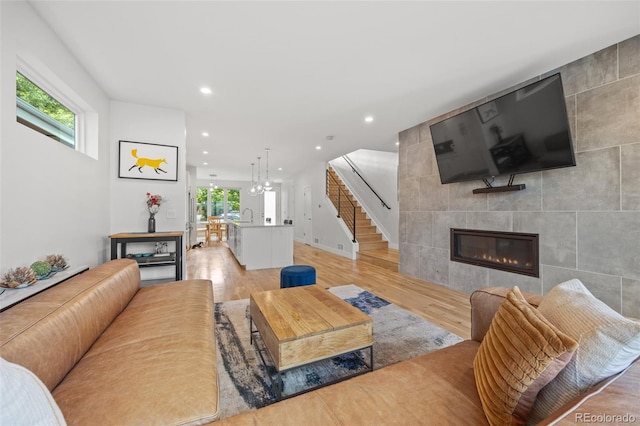 living room with sink, a tile fireplace, tile walls, a chandelier, and light wood-type flooring