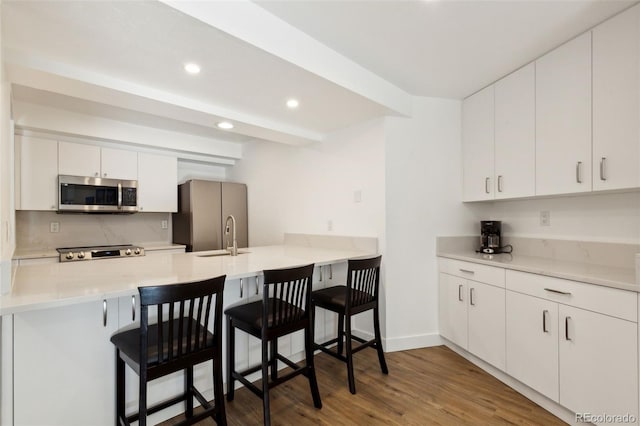 kitchen featuring white cabinetry, wood-type flooring, a kitchen breakfast bar, stainless steel appliances, and backsplash