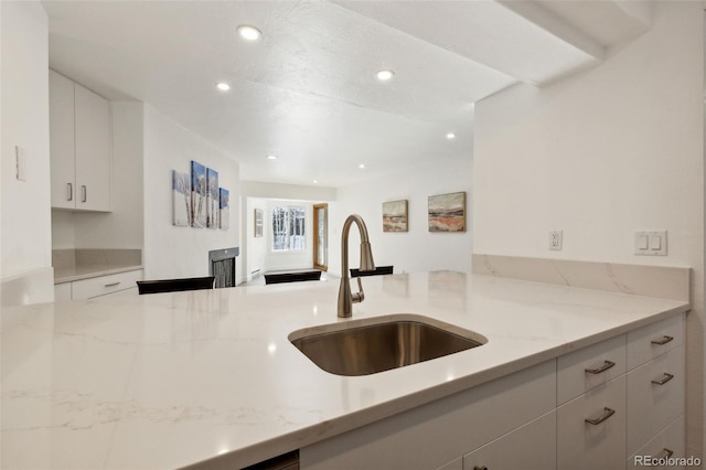 kitchen with white cabinetry, light stone countertops, and sink