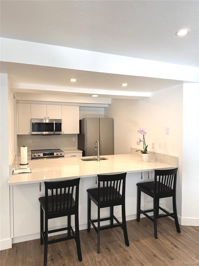 kitchen featuring dark wood-type flooring, stainless steel appliances, a kitchen breakfast bar, and kitchen peninsula