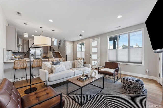 living area featuring light wood-type flooring, stairway, and visible vents