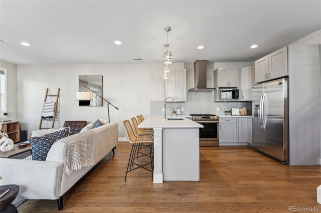 kitchen featuring open floor plan, light countertops, appliances with stainless steel finishes, wall chimney exhaust hood, and decorative light fixtures