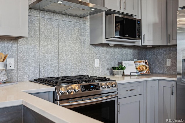 kitchen featuring tasteful backsplash, appliances with stainless steel finishes, light countertops, gray cabinetry, and wall chimney range hood