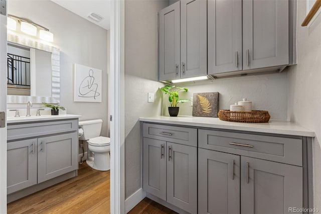 bathroom with baseboards, visible vents, toilet, wood finished floors, and vanity