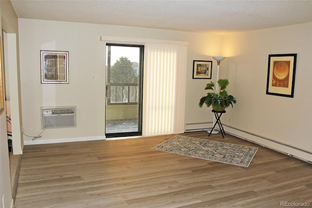 doorway with a wall mounted air conditioner, wood-type flooring, and a textured ceiling