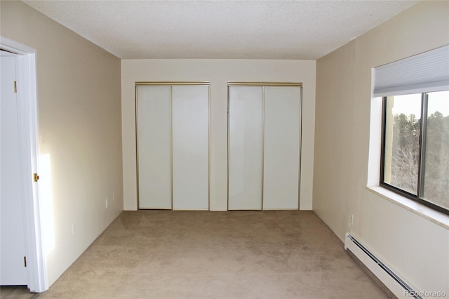 unfurnished bedroom with baseboard heating, light colored carpet, a textured ceiling, and two closets