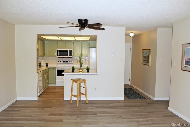 kitchen with tasteful backsplash, a kitchen breakfast bar, white appliances, green cabinetry, and a textured ceiling