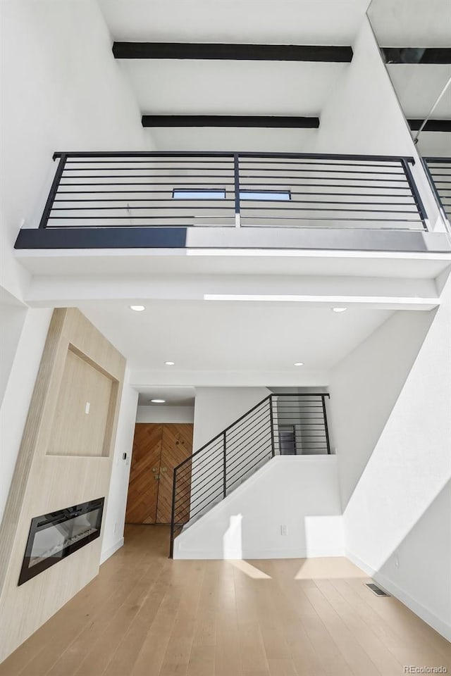 staircase with hardwood / wood-style floors, beam ceiling, and a high ceiling