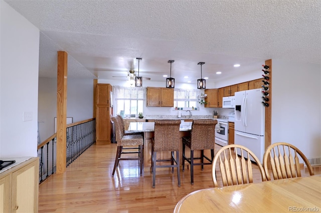 8217 Club Crest Dr, Arvada, CO 80005 - kitchen with white appliances, light wood-type flooring, a textured ceiling, a center island, and light countertops